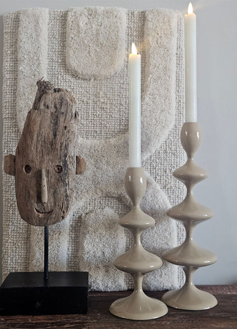 Light & Living kandelaar VIREEN zand 27cm met een witte kaars naast een houten masker ornament en een wit koraalornament op een houten bankje voor een schilderij