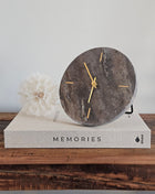 Light & Living klok Jenay bruin travertin op een koffietafelboek Memories met een witte paardenbloem op een houten ondergrond