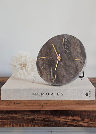 Light & Living klok Jenay bruin travertin op een koffietafelboek Memories met een witte paardenbloem op een houten ondergrond