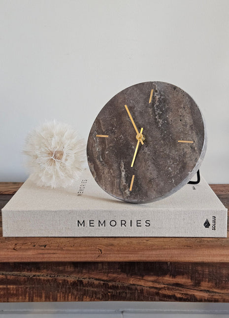 Light & Living klok Jenay bruin travertin op een koffietafelboek Memories met een witte paardenbloem op een houten ondergrond