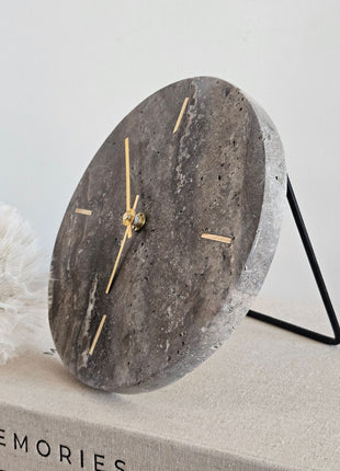 Zijaanzicht van een Light & Living klok Jenay bruin travertin op een zwart metalen standaard met een witte paardenbloem op de achtergrond