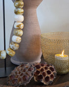 Close-up van bruine gedroogde lotuszaaddozen met ronde gaten naast onyx kralen en een goudkleurige lichthouder op hout
