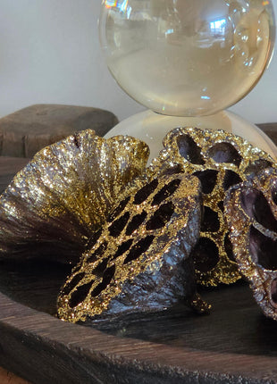 Close-up van bruin-gouden gedroogde lotuszaaddozen met glitter en ronde gaten naast een glazen kandelaar op hout