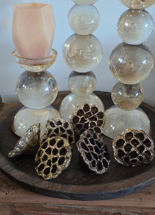 Vooraanzicht van bruin-gouden gedroogde lotuszaaddozen met glitter naast glazen bolkandelaars op houten dienblad