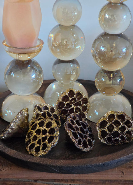 Vooraanzicht van bruin-gouden gedroogde lotuszaaddozen met glitter naast glazen kandelaars op een houten dienblad