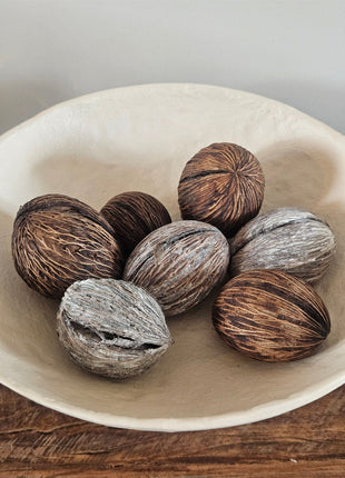 Zeven mintolla ballen in bruin en naturel met een geribbelde vezelige structuur in een witte ronde schaal op een houten ondergrond