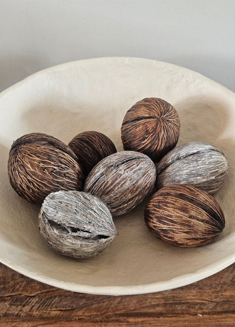 Zeven mintolla ballen in bruin en naturel met een geribbelde vezelige structuur in een witte ronde schaal op een houten ondergrond