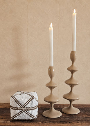 Kleine kralen offermand wit-goud met geometrisch kruispatroon op een houten ondergrond naast twee beige keramieken kandelaren met witte kaarsen