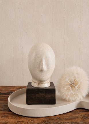Abstract hoofd beige met ovale vorm en uitstekende neus op een donkerbruine houten voet op een crème dienblad naast een witte gedroogde paardenbloem op een houten ondergrond