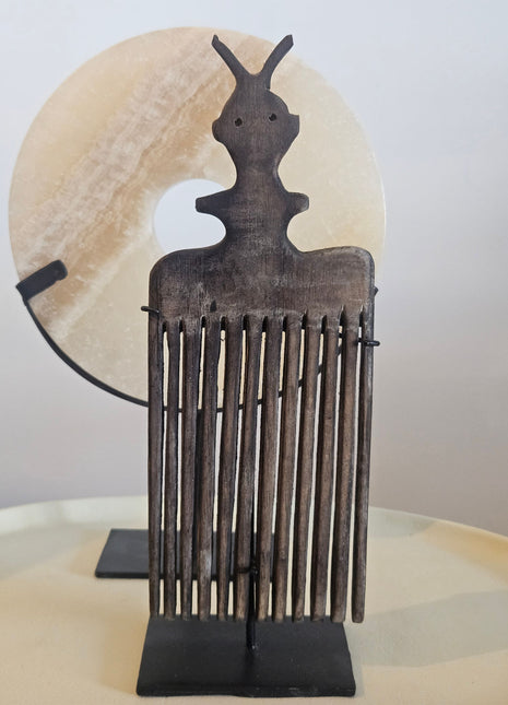Schelpenketting op zwarte standaard naast ornament kam op zwarte standaard in donkerbruin hout op witte achtergrond