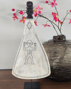 Ornament lepel wit naturel op zwarte standaard met gegraveerd figuur naast een donkere ronde vaas met roze bloesemtakken op een houten ondergrond