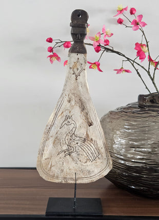 Lepel ornament naturel met gegraveerde pauw op een zwarte metalen standaard naast een grijze ronde vaas met roze bloesemtakken