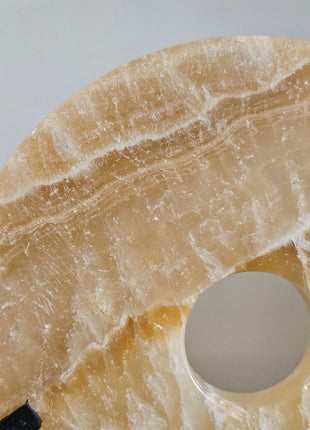 Ornament onyx beige natuursteen op zwarte standaard naast een schelpenketting op standaard op een houten ondergrond