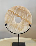Ornament onyx beige natuursteen op zwarte standaard naast een schelpenketting op standaard en een witte vaas op een houten ondergrond