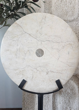 Rond marmeren ornament wit op een zwarte metalen standaard met een witte geribde achtergrond