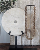 Rond marmeren ornament wit op een zwarte metalen standaard naast een houten kralenketting op een houten ondergrond