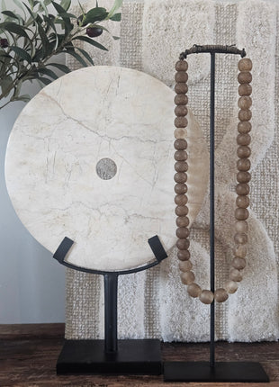 Rond marmeren ornament wit op een zwarte metalen standaard naast een houten kralenketting op een houten ondergrond