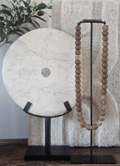 Rond marmeren ornament wit op een zwarte metalen standaard naast een houten kralenketting op een houten ondergrond