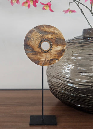 Ronde houten schijf bruin naturel met gegraveerd zonmotief op een zwarte metalen standaard