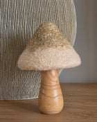 Paddenstoel Golden Glitter met een crème bouclé bovenkant met gouden glitterrand op een naturel houten steel voor een geribbelde grijze vaas op een houten tafel