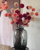 Complete glazen Vase The World Kara Tasman vaas met pompom zijdebloemen in pink, champagne en burgundy in woonkamer met schilderij op achtergrond