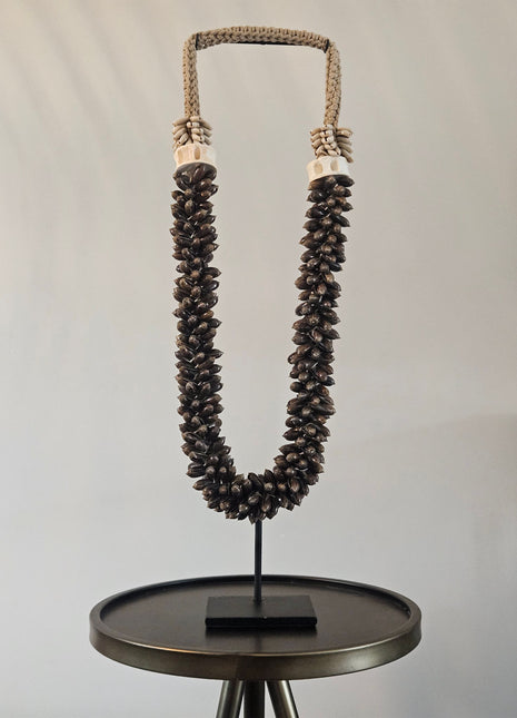 Schelpenketting bruin L op zwarte metalen standaard met donkerbruine ovale schelpen en gevlochten jute band op een witte achtergrond