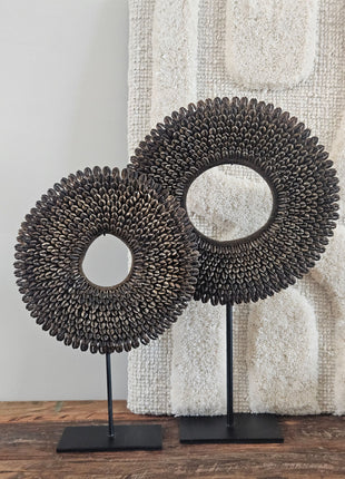 Drie schelpenkettingen bruin op zwarte standaarden in maat S M en L naast een bronzen kralenketting op standaard op een houten ondergrond