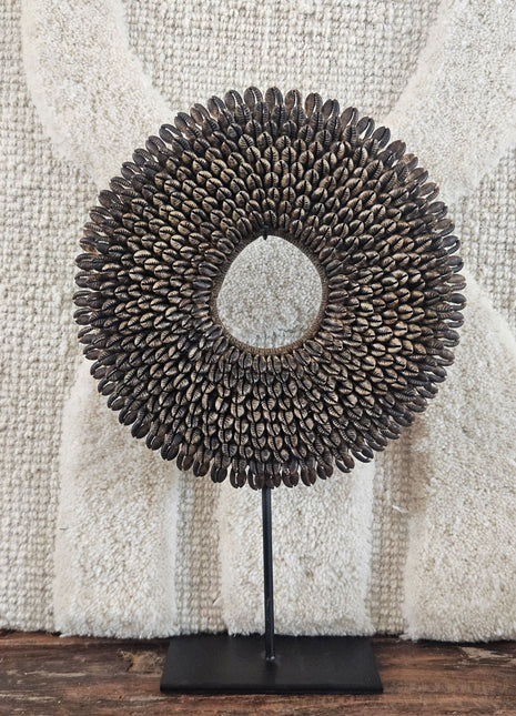 Schelpenketting bruin M op zwarte metalen standaard met bruine kauri-schelpen en gevlochten jute band op een witte achtergrond