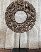 Schelpenketting bruin M op zwarte metalen standaard met bruine kauri-schelpen en gevlochten jute band op een witte achtergrond