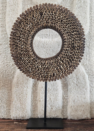 Schelpenketting bruin M op zwarte metalen standaard met bruine kauri-schelpen en gevlochten jute band op een witte achtergrond