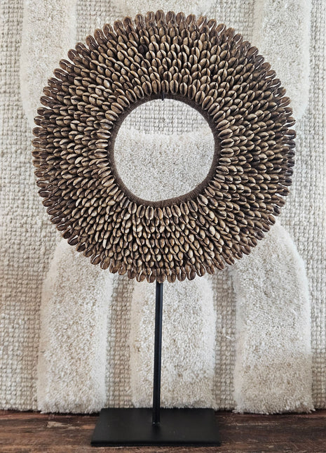 Schelpenketting bruin M op zwarte metalen standaard met bruine kauri-schelpen en gevlochten jute band op een witte achtergrond