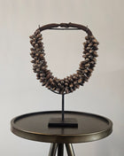 Schelpenketting bruin M op zwarte metalen standaard met bruine kauri-schelpen en gevlochten jute band op een witte achtergrond