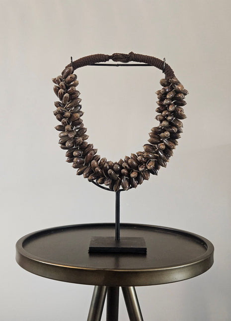 Schelpenketting bruin M op zwarte metalen standaard met bruine kauri-schelpen en gevlochten jute band op een witte achtergrond