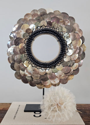 Schelpenketting gepolijste schelpen L op zwarte standaard naast twee taupe keramieke kandelaars op een houten dressoir voor een crème schilderij met boogmotief