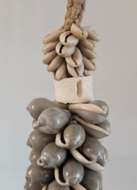 Close-up van schelpenketting grijs met ronde grijze schelpen witte kauri-schelpen en een wit rechthoekig been ornament op een gevlochten jute band