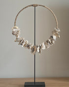 Schelpenketting op standaard Placuna met witte schelpen op een naturel houten standaard op een lichte ondergrond