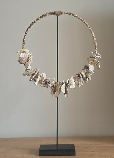 Schelpenketting op standaard Placuna met witte schelpen op een naturel houten standaard op een lichte ondergrond