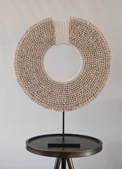 Schelpenketting wit-beige XL op zwarte metalen standaard met kauri-schelpen en gevlochten band op een witte achtergrond