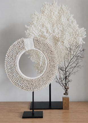 Schelpenketting wit-beige L op zwarte metalen standaard op een houten bijzettafel voor een witte muur