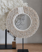 Schelpenketting wit-beige L op zwarte metalen standaard op een houten dressoir naast een zwarte houten kam op standaard en een beige onyx schijfornament op standaard