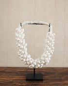 Schelpenketting wit M op zwarte metalen standaard met witte kauri-schelpen en gevlochten witte band op een witte achtergrond