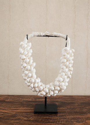 Schelpenketting wit M op zwarte metalen standaard met witte kauri-schelpen en gevlochten witte band op een witte achtergrond
