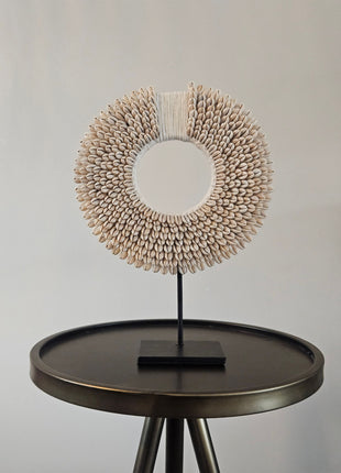 Schelpenketting wit S op zwarte metalen standaard met kauri-schelpen en gevlochten witte band op een witte achtergrond