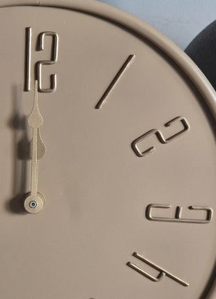 Close-up van beige Liva tafelklok met gladde afwerking en goudkleurige wijzers en cijfers tegen grijs