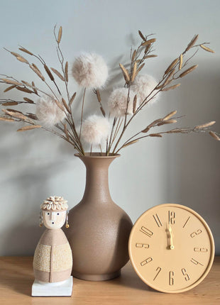 Vooraanzicht van beige Liva tafelklok met gladde afwerking naast een taupe halsvaas en Namji pop op hout