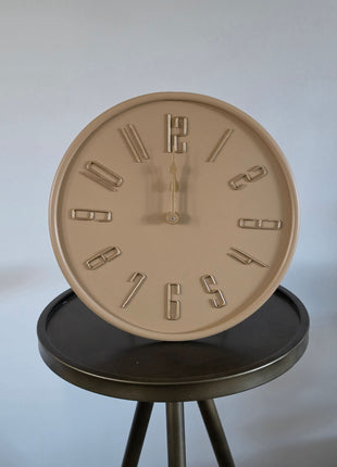 Vooraanzicht van beige Liva tafelklok met gladde afwerking en goudkleurige cijfers op een rond metalen tafeltje