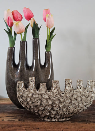 Tulpenvaas bruin speckled aardewerk H 32 cm naast tulpenvaas speckled crème H 15.5 cm met roze-rode tulpen op een houten ondergrond voor een lichtgrijze muur