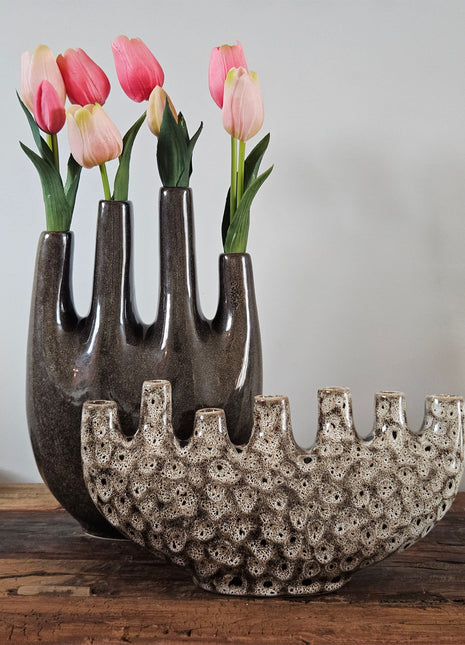 Tulpenvaas bruin speckled aardewerk H 32 cm naast tulpenvaas speckled crème H 15.5 cm met roze-rode tulpen op een houten ondergrond voor een lichtgrijze muur