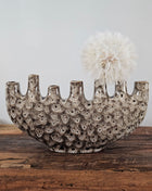 Tulpenvaas speckled crème aardewerk H 15.5 cm met zeven kleine halsopeningen en een halfronde boogvorm op een houten ondergrond voor een lichtgrijze muur