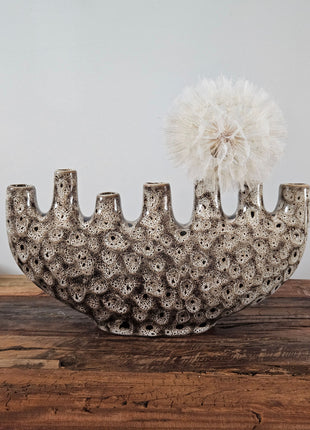 Tulpenvaas speckled crème aardewerk H 15.5 cm met zeven kleine halsopeningen en een halfronde boogvorm op een houten ondergrond voor een lichtgrijze muur
